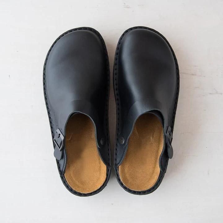 Draufsicht auf ein Paar schwarze Leder-Clogs mit geschwungenem Fußbett in Hellbraun und seitlicher Schnalle 9