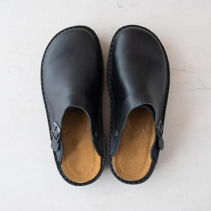 Draufsicht auf ein Paar schwarze Leder-Clogs mit geschwungenem Fußbett in Hellbraun und seitlicher Schnalle 9