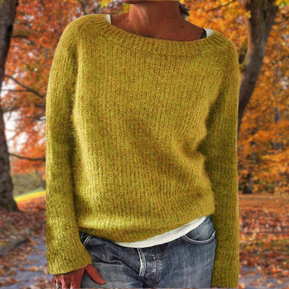 Senfgelber Strickpullover mit rundem Ausschnitt, getragen von einer Frau mit Jeans und weißem Shirt vor herbstlichem Laub. 1