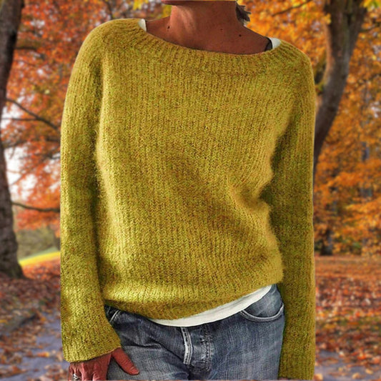 Senfgelber Strickpullover mit rundem Ausschnitt, getragen von einer Frau mit Jeans und weißem Shirt vor herbstlichem Laub. 1