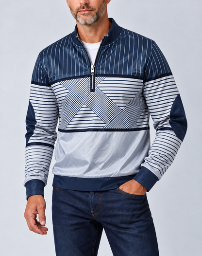 Mann mit grauem Bart trägt den marineblau-weiß gestreiften Pullover mit halbem Reißverschluss zu dunkler Jeans, Hand in der Hosentasche. 1