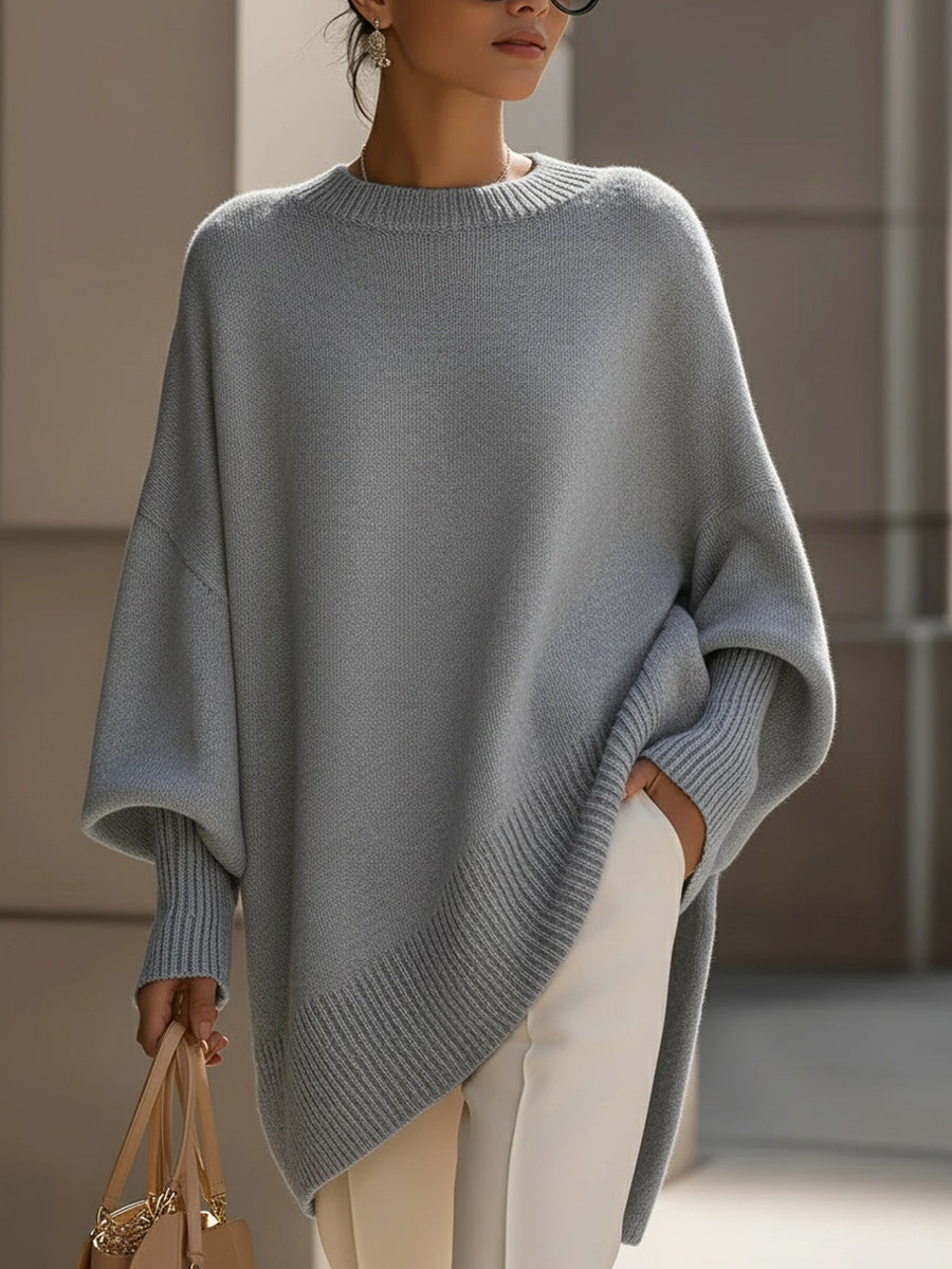 Grauer Strickponcho in lockerem Schnitt, getragen mit weißer Hose und beiger Handtasche 10