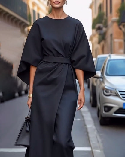 Schwarzes Wickelkleid mit weiten Ärmeln und Taillengürtel, von vorn getragen mit Ohrringen und kleiner schwarzer Tasche auf einer Straße. 6