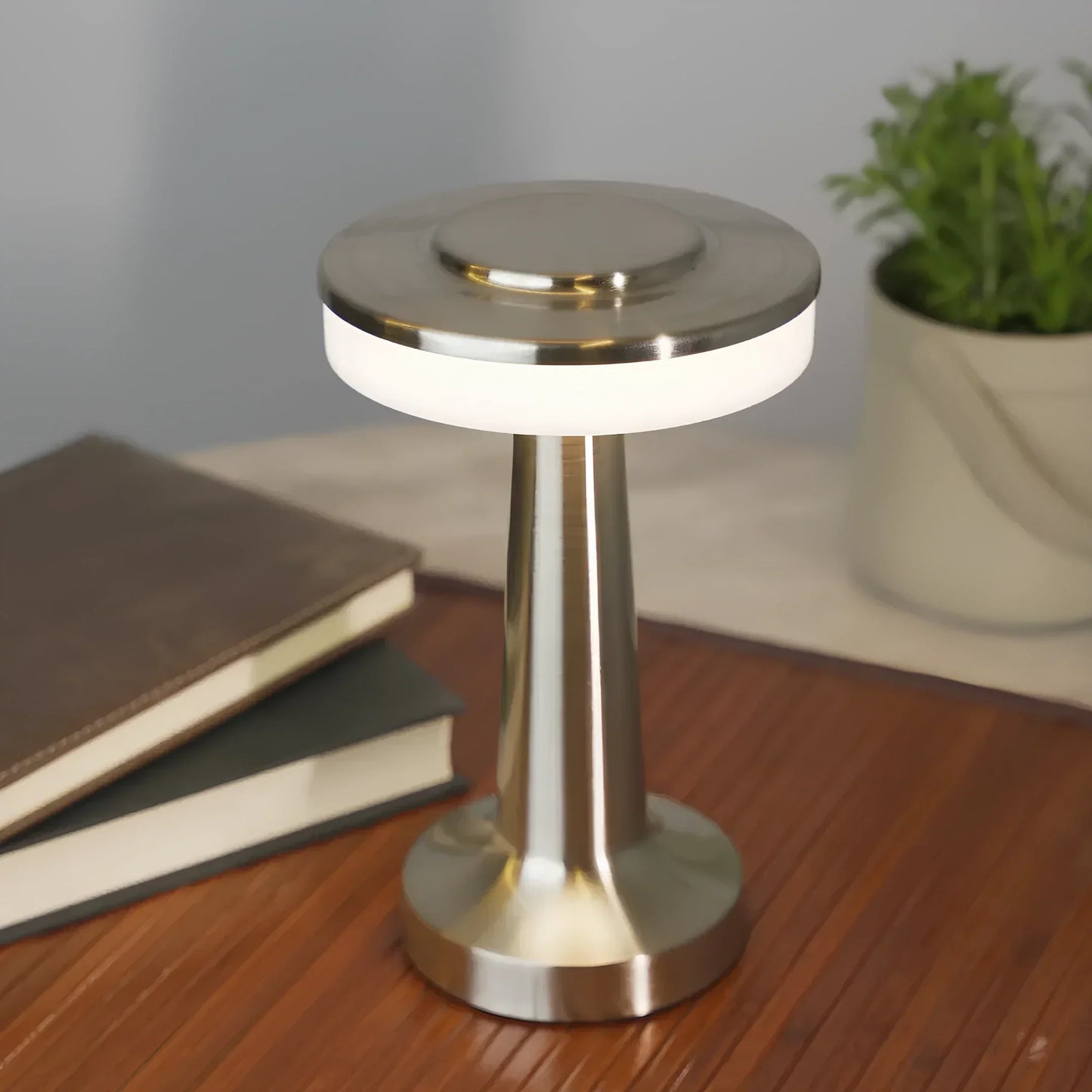 Moderne LED-Tischlampe aus Edelstahl, energiesparend, auf Holztisch mit Büchern und Pflanze.
