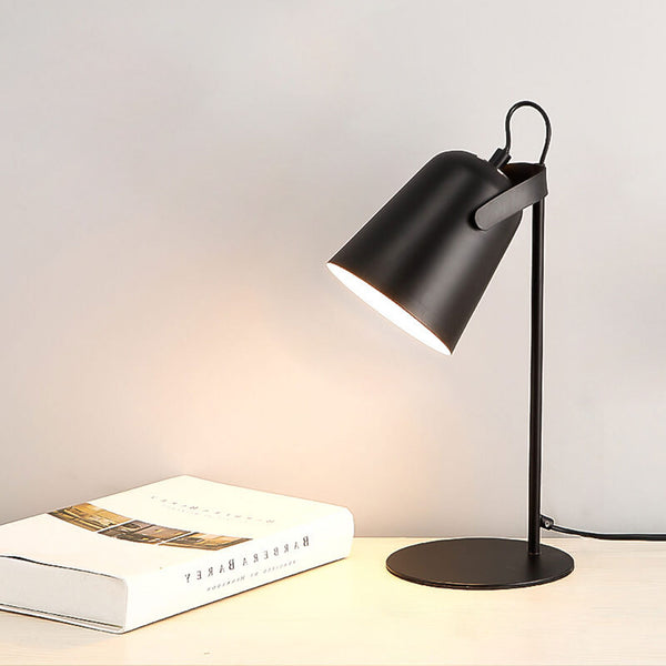 Schwarze Tischlampe mit schräg gestelltem Schirm leuchtet warm auf einem hellen Tisch neben einem aufgeschlagenen Buch. 12