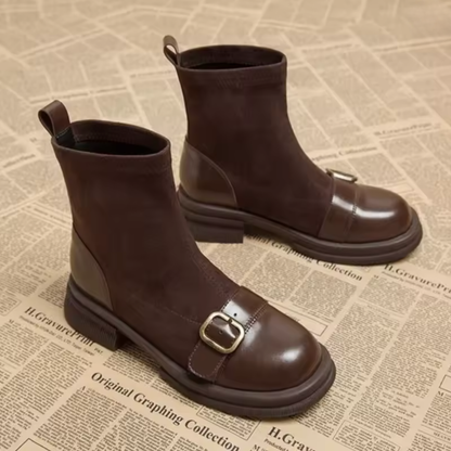 Zwei braune Wildlederstiefel mit glänzender Lederkappe, goldfarbener Schnalle und kräftiger Sohle, weitere Ansicht.