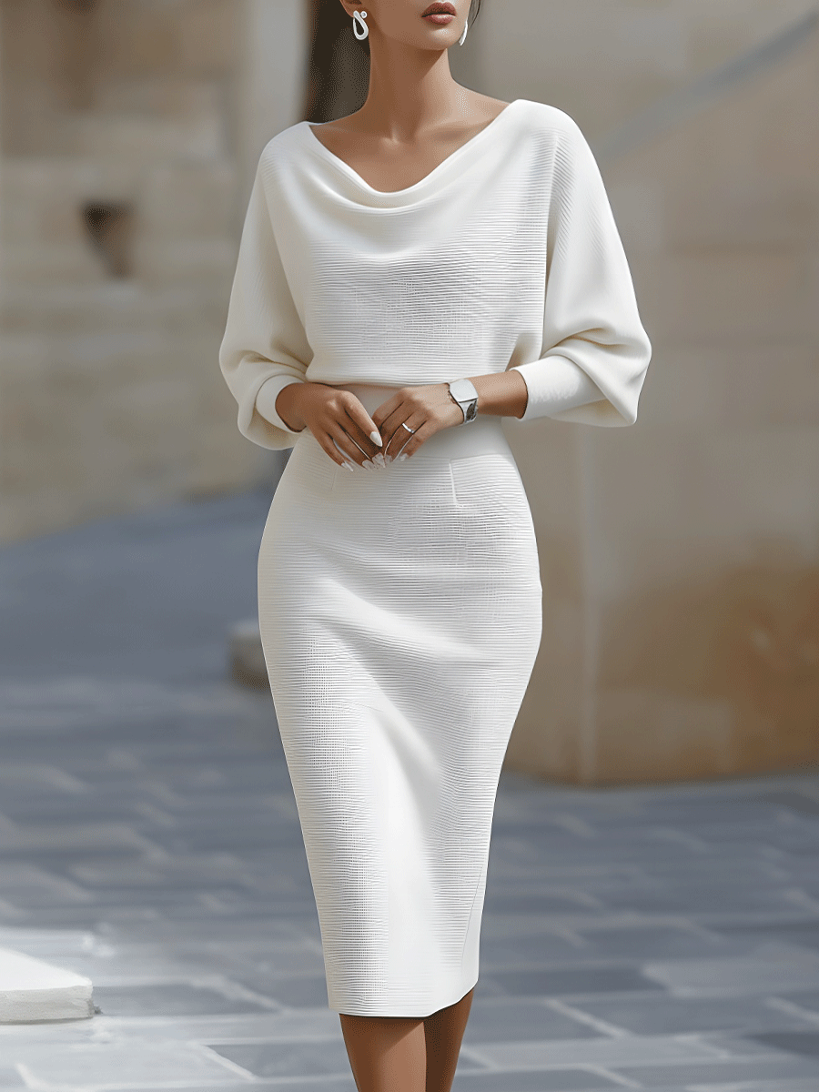 Frontansicht: Model in weißem, gerippt gestricktem Midikleid mit drapiertem Ausschnitt und weiten Dreiviertelärmeln vor heller Steinkulisse. 2