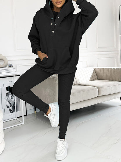 Frau in schwarzem Hoodie und Leggings, weiße Sneakers, modernes Wohnzimmer, Freizeitmode.