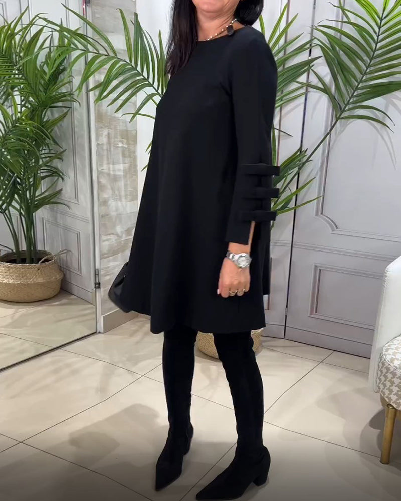 Frau in schwarzem Kleid mit langen Ärmeln, schwarze Stiefel, moderne Inneneinrichtung, Pflanzen.