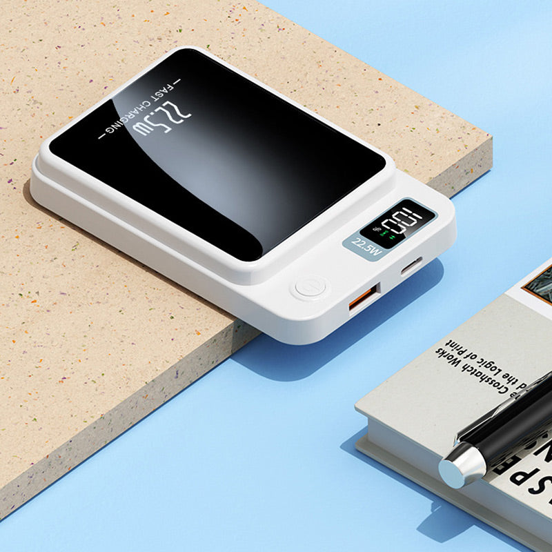 Weißes Ladegerät mit USB-Anschlüssen, Einschalttaste und Display neben einem Buch mit Stift.