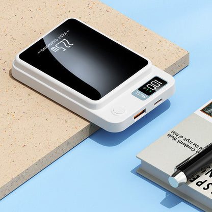 Weißes Ladegerät mit USB-Anschlüssen, Einschalttaste und Display neben einem Buch mit Stift.