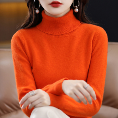 Orangefarbener Rollkragenpullover am sitzenden Model mit heller Hose.