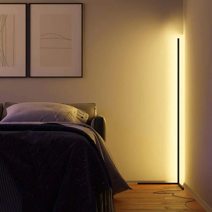 Stehlampe in gelblichem Licht in der Zimmerecke neben einem Bett, daneben zwei gerahmte Bilder 4