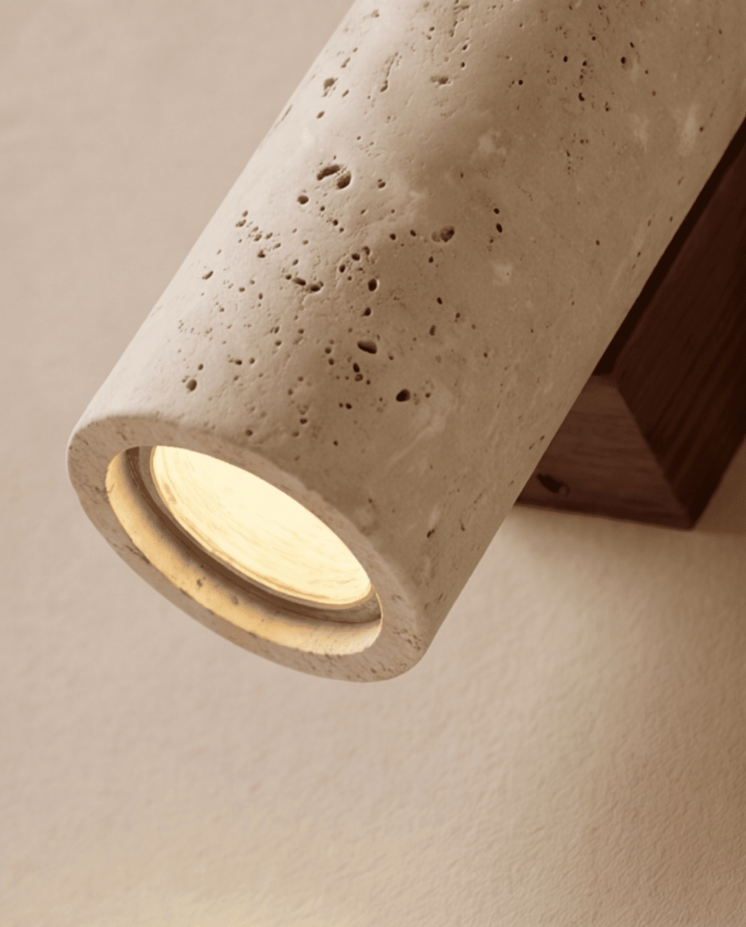 Nahaufnahme der unteren Lichtöffnung des Travertinzylinders mit eingesetztem Leuchtmittel und dunkler Holzhalterung dahinter 5