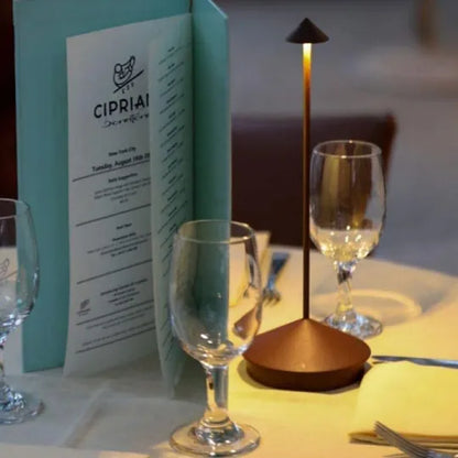 Tischlampe LED modern, bronzefarben, neben Weingläsern und Speisekarte im Restaurant.