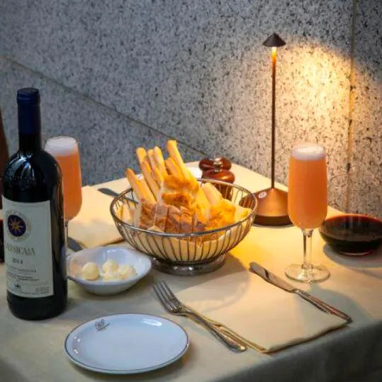 Esstisch mit Rotwein, Brot, Butter, zwei Gläsern Saft, Tischlampe, elegantes Abendessen.