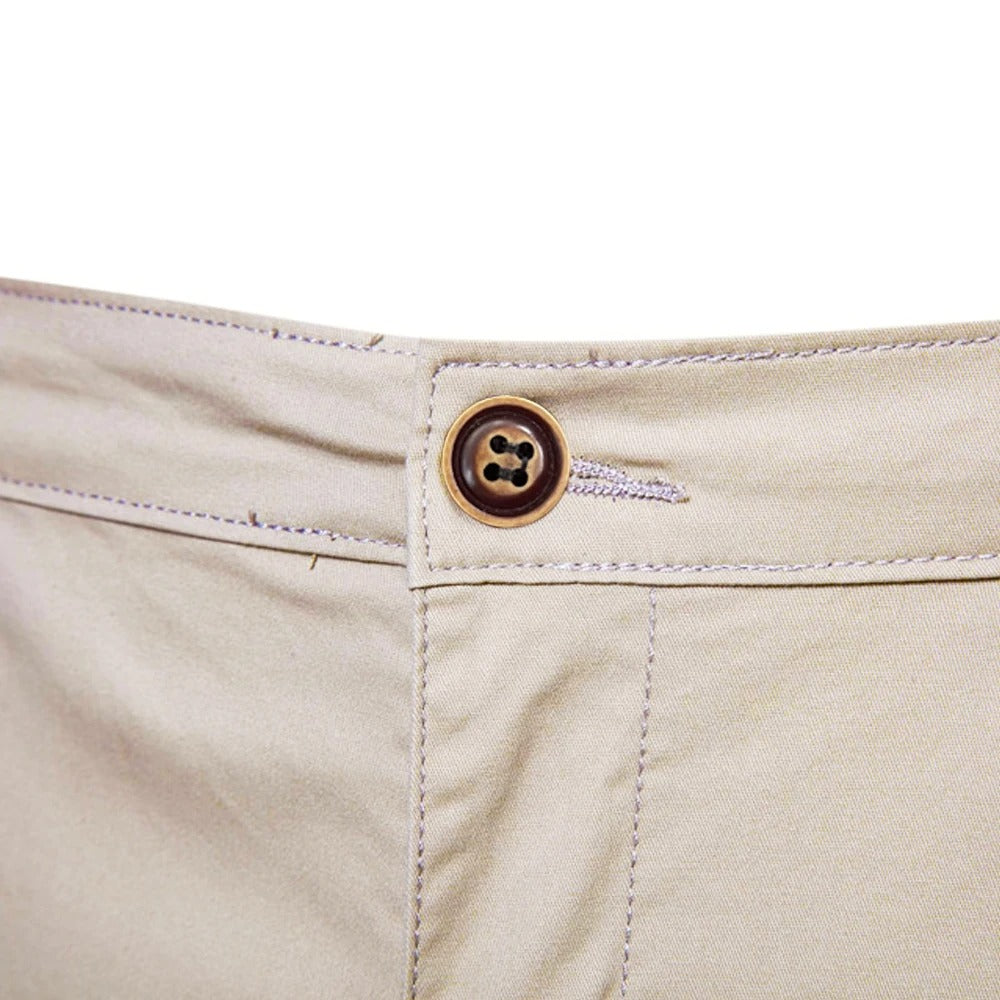 Nahaufnahme des braunen Knopfs mit Knopfloch am Bund der beigen Shorts, umgeben von hellen Steppnähten. 5