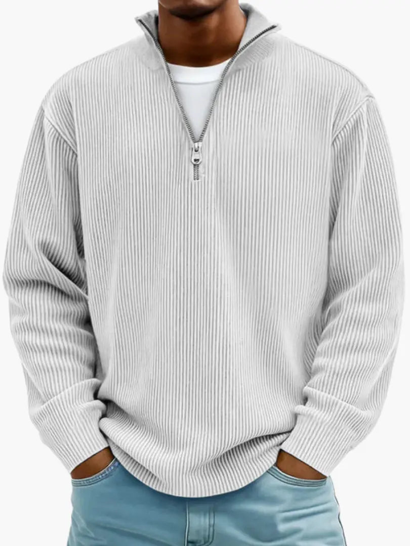 Gerippter Pullover in Hellgrau mit Stehkragen und Reißverschluss, getragen von einem Model mit weißem Shirt darunter.