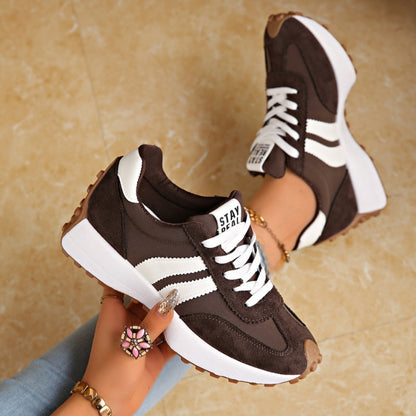 Dunkelbraune Sneaker mit weißen Streifen und Plateausohle, in der Hand gehalten, Fuß mit Armband im Hintergrund 3