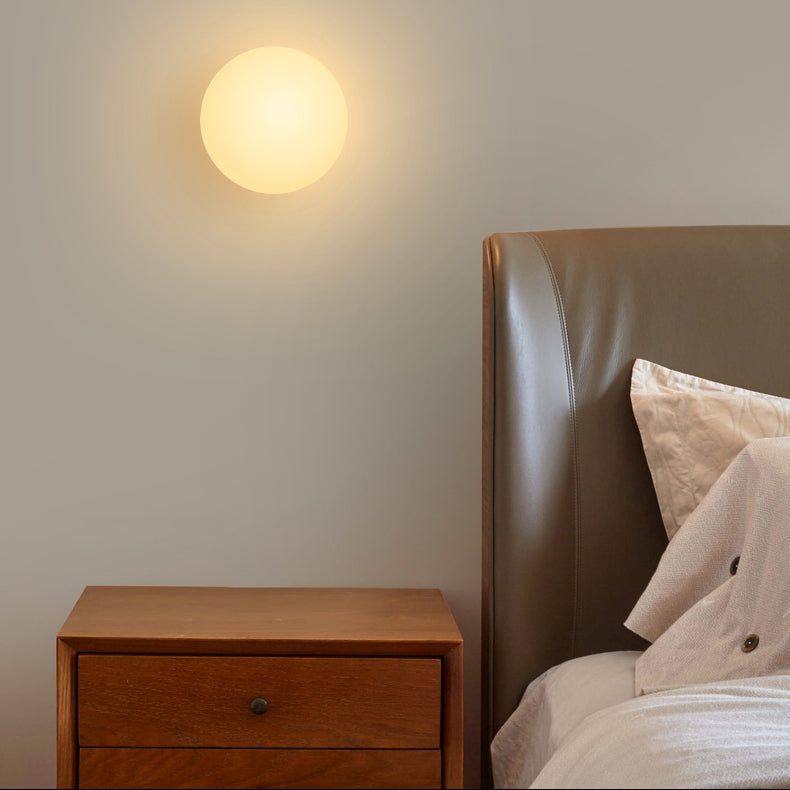 Warm leuchtende Kugelleuchte an der Wand über einem Holznachttisch neben einem Bett mit Lederkopfteil 2