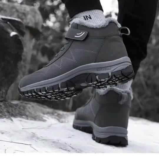 Graue Stiefel getragen auf Schnee, ein Fuß angehoben und die profilierte Sohle von unten zu sehen 8