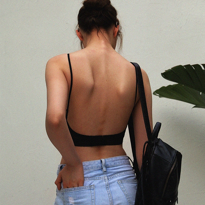 Rückansicht einer Frau im schwarzen BH mit tiefem, rückenfreiem Ausschnitt und dünnen Trägern, dazu Jeans und schwarzer Rucksack. 2