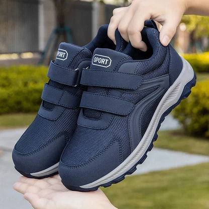 Hände halten ein Paar blaue Klettschuhe vor einer grünen Gartenkulisse in die Höhe 12