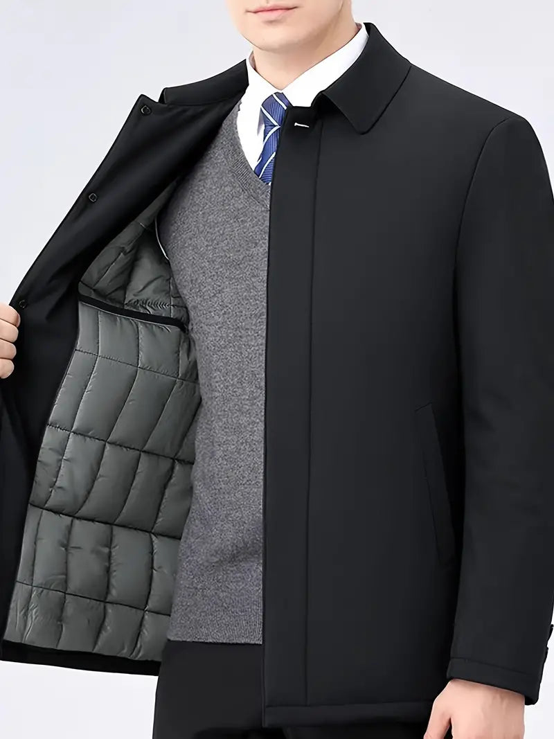 Mann in schwarzem Mantel mit grauem Innenfutter, grauem Pullover und blauer Krawatte.