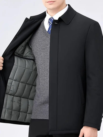 Mann in schwarzem Mantel mit grauem Innenfutter, grauem Pullover und blauer Krawatte.