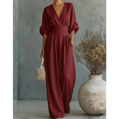 Weinroter Damen-Jumpsuit mit breitem Taillenband und Seitentaschen neben einer Vase mit Trockenblumen, front view