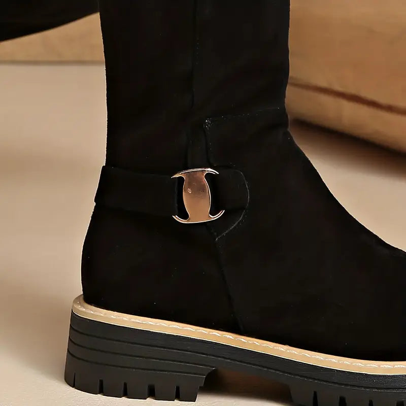 Detail der schwarzen Stiefel mit goldfarbener Zierschnalle, heller Ziernaht und dicker Profilsohle.
