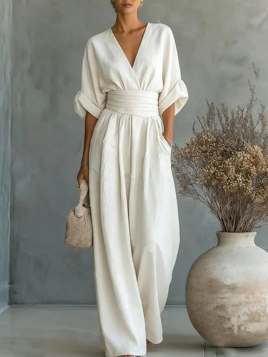 Cremeweißer Damen-Jumpsuit mit V-Ausschnitt und weitem Hosenbein neben einer Vase mit getrockneten Blumen