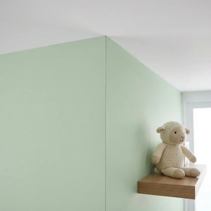 Detailaufnahme einer sauberen, geraden Farbkante an einer hellgrünen Wand mit Stofflamm auf einem Holzregal 5