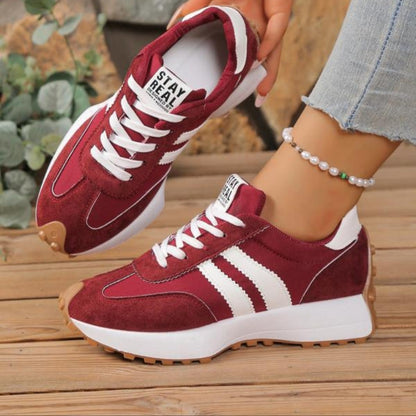 Weinrote Wildleder-Sneaker mit weißen Streifen, getragen zu Jeans und Perlen-Fußkettchen auf Holzboden 4