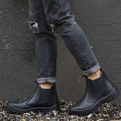 Person in grauer Jeans trägt schwarze Chelsea-Stiefel und steht auf glänzenden Metallspänen vor dunkler Wand 7