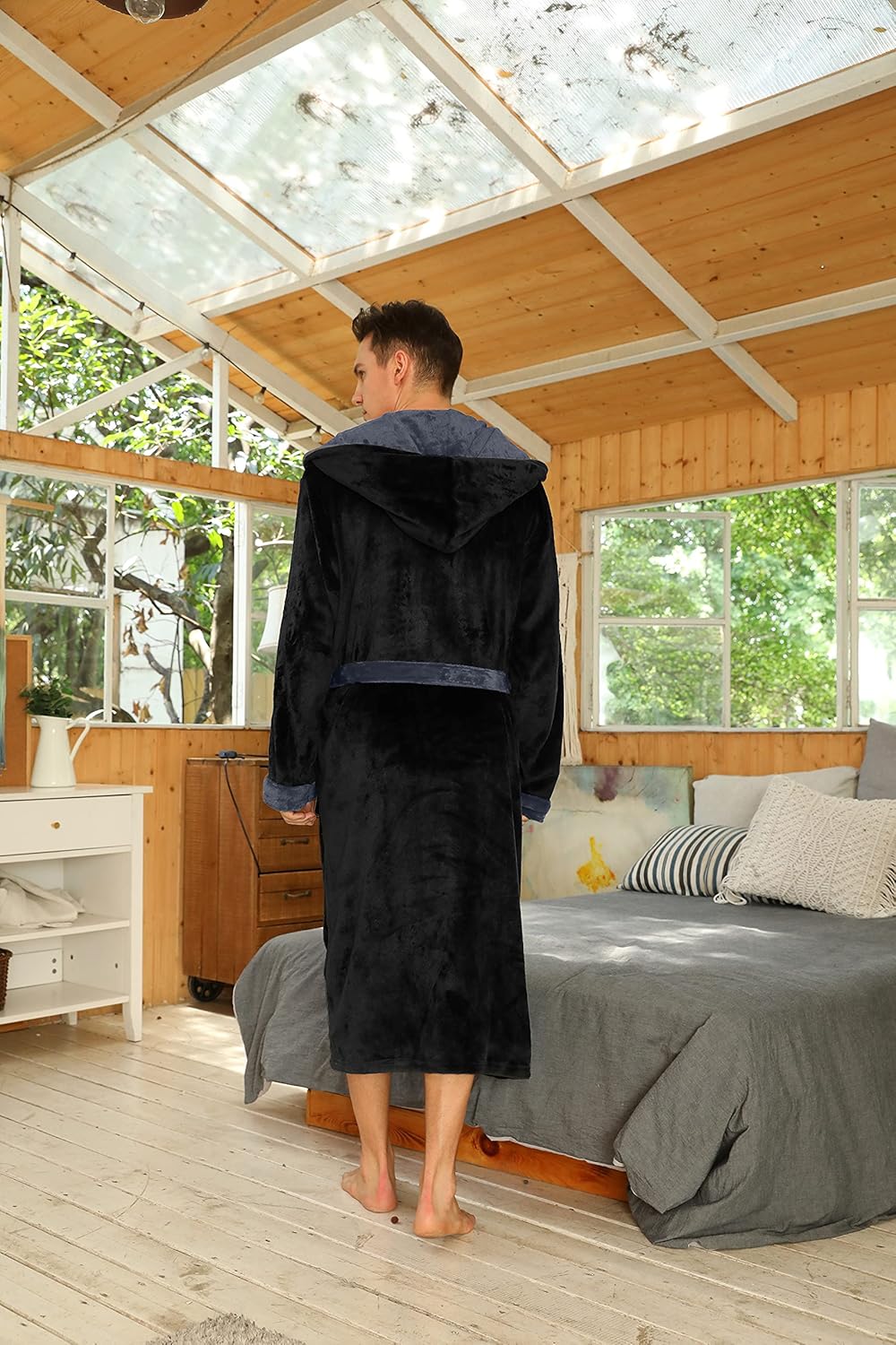 Mann im schwarzen Fleece-Bademantel mit Kapuze im Schlafzimmer, gemütliche Morgenroutine.