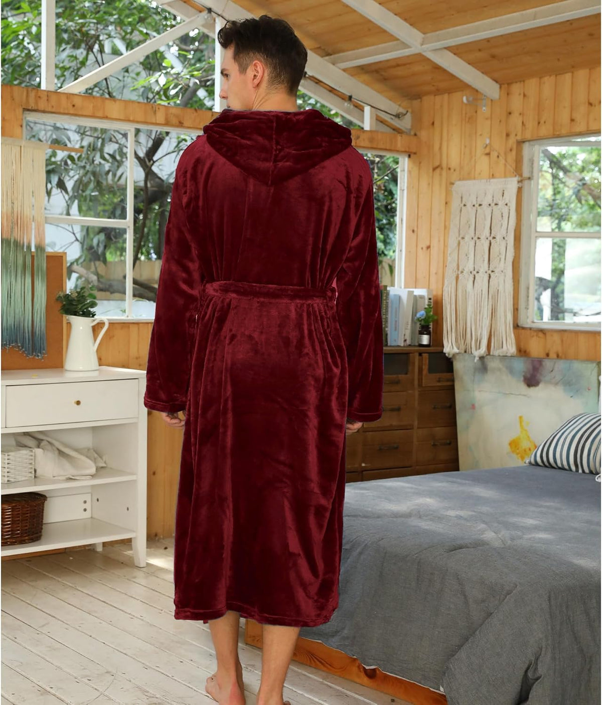 Mann im roten Fleece-Bademantel mit Kapuze im Schlafzimmer, gemütliche Morgenroutine.