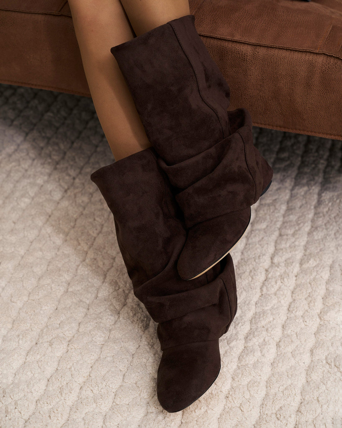 Getragene Stiefel an Beinen in Strumpfhose auf einem braunen Sofa, zweite Ansicht.