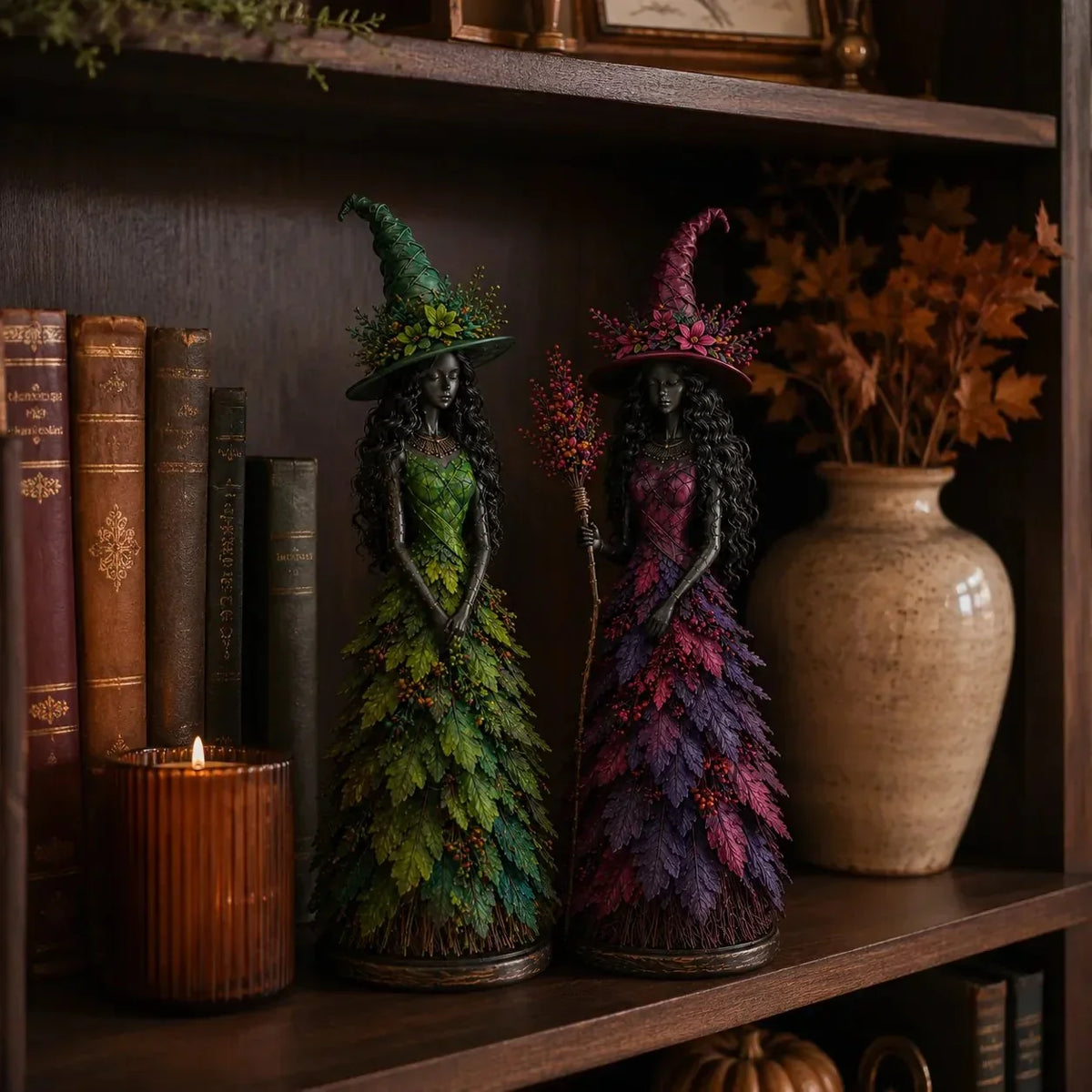 Grüne und violette Hexenfigur nebeneinander auf einem dunklen Bücherregal, neben Büchern, Kerzenglas und einer Keramikvase mit Herbstlaub. 4