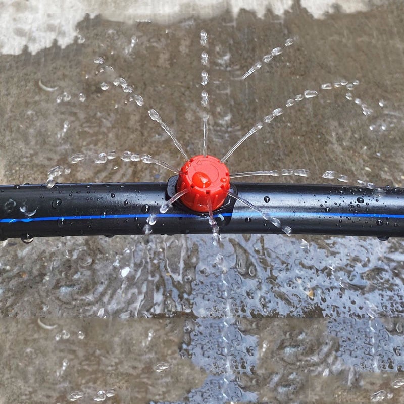 Roter Tropfer auf einem schwarzen Schlauch mit blauem Streifen, der Wasser in feinen Strahlen versprüht.
