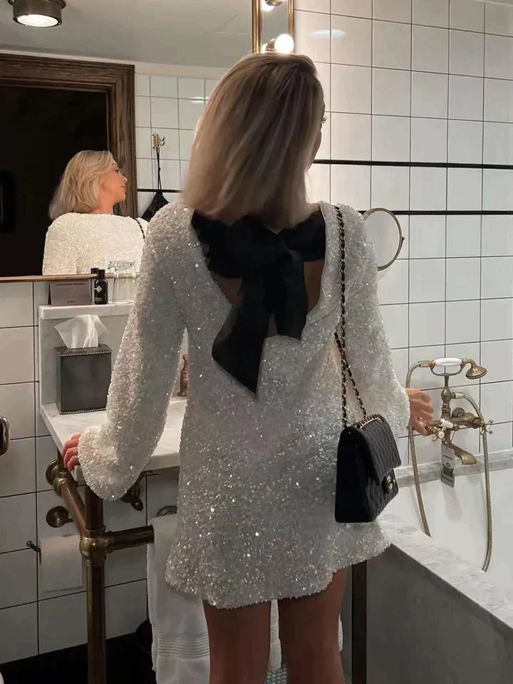 Frau im weißen Paillettenkleid mit schwarzer Schleife im Badezimmer, elegante Abendmode.
