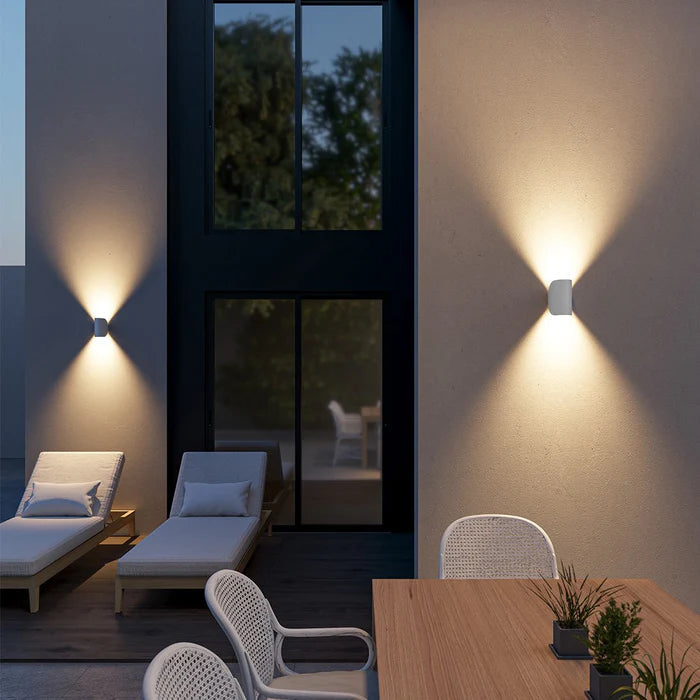 Weiße Wandleuchten mit Licht nach oben und unten an der Hauswand einer Terrasse am Abend.