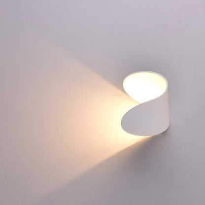 Nahaufnahme einer weißen Wandleuchte, die einen warmen Lichtkegel schräg auf die helle Wand wirft.