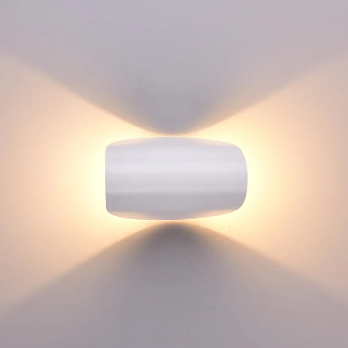 Frontansicht einer weißen Wandleuchte, die warmes Licht gleichmäßig nach oben und unten an die Wand strahlt.