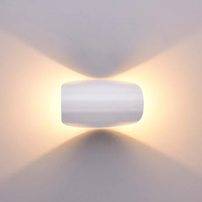 Frontansicht einer weißen Wandleuchte, die warmes Licht gleichmäßig nach oben und unten an die Wand strahlt.