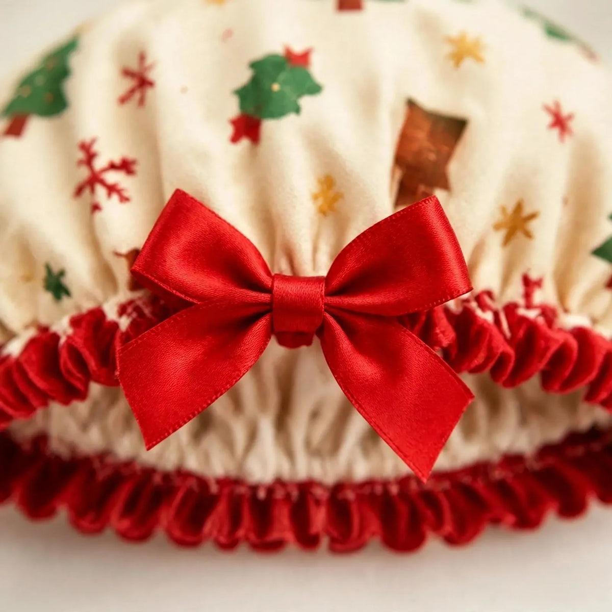 Nahaufnahme der cremefarbenen Duschhaube mit Weihnachtsmotiven, roter Satinschleife und gerüschtem roten Rand 3