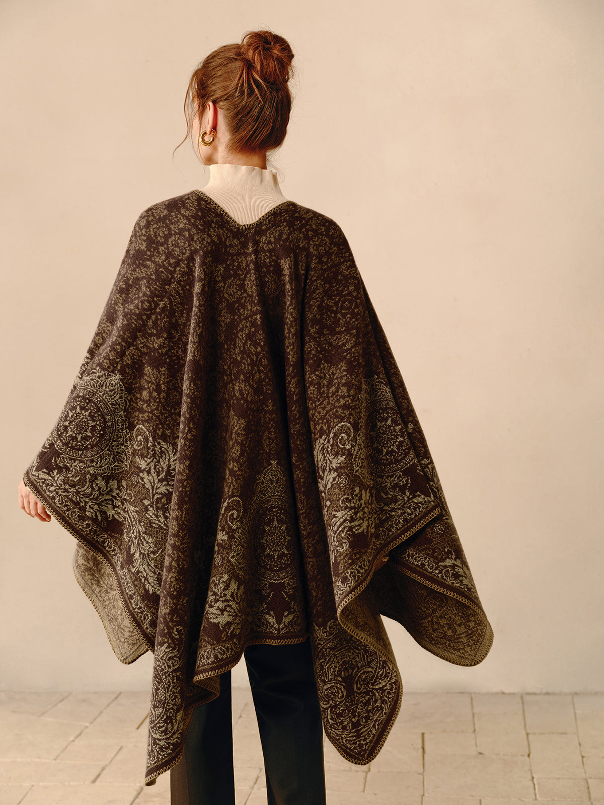 Frau trägt braunen Poncho mit Paisley-Muster, elegantes Herbstoutfit, Rückansicht.