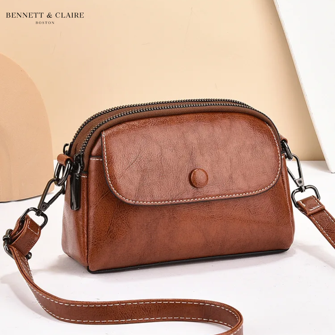 Umhängetasche aus Kunstleder in Cognacbraun mit Klappe, Druckknopf und Reißverschlussfächern.