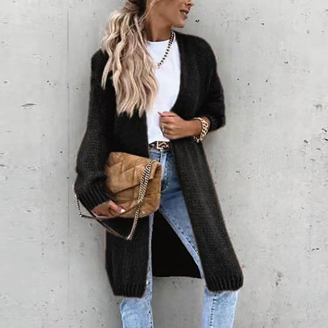 Frau in schwarzem Strickmantel, weißem T-Shirt, blauer Jeans, brauner Tasche, lässiger Look.