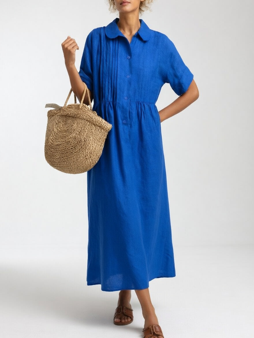 Das Hemdkleid in leuchtendem Königsblau, getragen mit einer Hand an der Hüfte und einer Strohtasche am Arm.